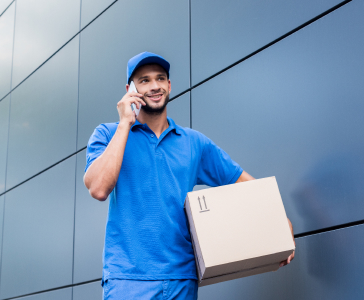 smiling-delivery-man-with-cardboard-box-talking-by-2022-12-16-17-35-50-utc-1.jpg